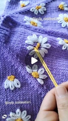 someone is knitting flowers on a purple knitted sweater with yellow and white crochet