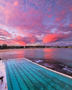 an outdoor swimming pool with blue water and pink clouds