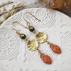 You can almost smell the crisp fall air with these boho autumn earrings. dainty brass disc's are hammered to perfection and adorned with rich green Czech glass and pumpkin orange fall leaves. Finished with 14k gold plated earring hooks. - Gorgeous boho autumn styling - Brass materials - Czech glass beads - 14k gold plated earring hooks with rubber backs included Earthy Brass Jewelry With Ear Wire, Nickel-free Brass Earthy Earrings, Earthy Nickel-free Brass Earrings, Earthy Nickel-free Brass Jewelry, Bohemian Copper Earrings With Hammered Detail, Bohemian Hammered Copper Earrings, Earthy Brass Dangle Earrings, Earthy Bronze Brass Earrings, Bohemian Hammered Dangle Earrings