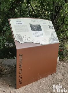 an informational sign on the side of a dirt road with trees in the background