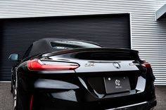 the rear end of a black sports car parked in front of a garage door with roller shutters