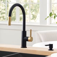 a black kitchen faucet with gold handles and brass spout, in front of a white dining room table