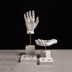 two white mannequins with gold rings and jewelry on display in front of a black background