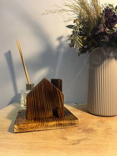 a white vase filled with purple flowers next to a wooden house shaped pen holder on top of a table