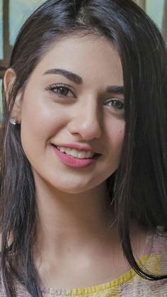 a woman with long dark hair smiling at the camera while wearing a yellow shirt and earrings