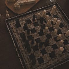 a game of chess is set up on a table next to some wine glasses and cheese