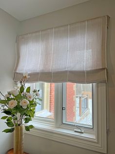 a vase with flowers on a table in front of a window that has the blinds closed