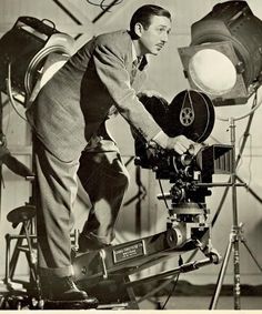 an old black and white photo of a man with a camera on a tripod