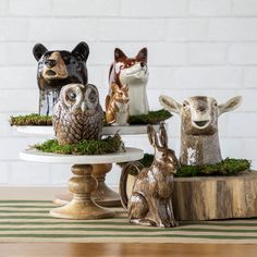 four small ceramic animals sitting on top of a cake plate with moss and pine cones