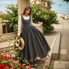 a woman in a dress and hat standing on the side walk with flowers around her