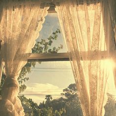 the sun shines through an open window with white curtains and green leaves on it