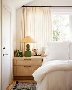 a bed with white sheets and pillows in a bedroom next to a lamp on a dresser