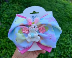 a hand holding up a blue and pink bow with a bunny on it's head