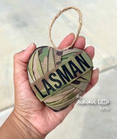 a hand holding an ornament with the word lasman on it in camouflage