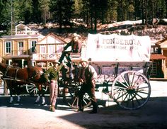 two men are standing next to a horse drawn carriage in front of small wooden buildings