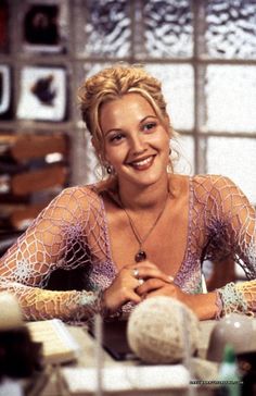 a woman sitting at a table smiling and wearing a fish net top shirt with her hands on her chest