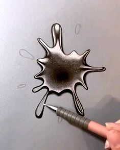 a person is drawing on the wall with black ink and silver paint while holding a pen