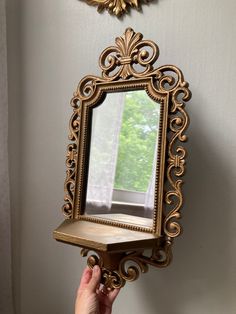 a person holding a mirror in front of a wall mounted shelf with a clock on it