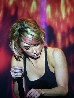 a woman holding a cell phone in front of a red and purple wall with lights on it