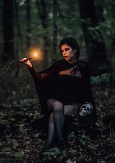 a woman sitting on the ground holding a lit candle in her hand and wearing a black dress