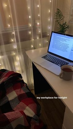 an open laptop computer sitting on top of a white desk next to a window covered in fairy lights