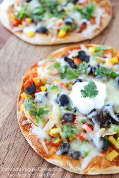 two small pizzas with toppings sitting on top of a wooden table next to each other