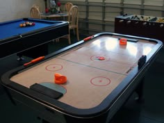 two air hockey tables with orange cups on them in a room filled with chairs and table tennis