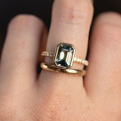 a woman's hand holding a ring with an emerald stone in the middle and diamond band around it