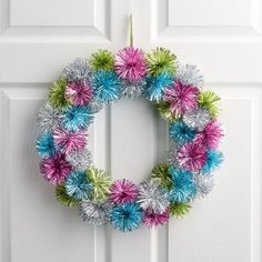 a colorful wreath is hanging on the front door with tinsel balls around it and an ornament in the middle