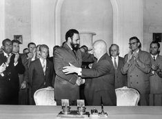 a group of men standing around a table in front of a man with his arms crossed