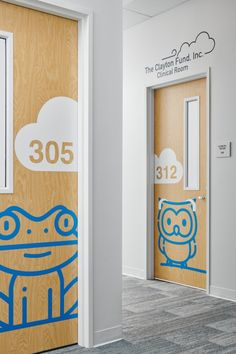 two wooden doors with blue drawings on them in an office building, the door is open