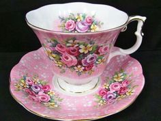 a pink tea cup and saucer with flowers on the side, sitting on a black surface