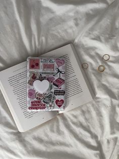 an open book sitting on top of a bed next to two gold rings and a pair of earrings