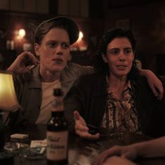 two women sitting at a table with bottles of alcohol in front of them and one woman holding her arm around the other