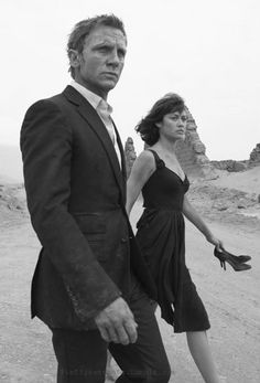 a man and woman walking down a dirt road in front of some ruins on the other side