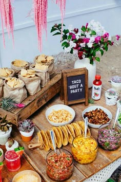 an assortment of taco bar food on a wooden table with pink flowers in the background