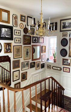 a staircase with many framed pictures on the wall and a chandelier hanging above it