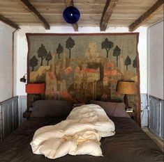 an unmade bed in front of a tapestry on the wall