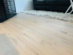 an empty living room with a black couch and white rugs on the hardwood floor