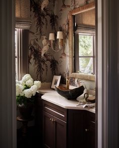 a bathroom sink sitting under a window next to a vase with white flowers on it