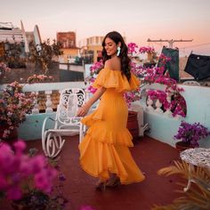 a woman in an orange dress is standing on a balcony with flowers and potted plants