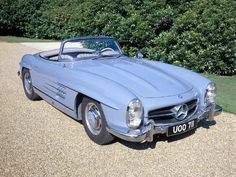 an old blue mercedes sports car parked on gravel