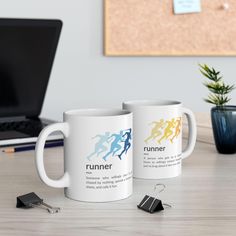 two white coffee mugs sitting on top of a wooden table next to a laptop