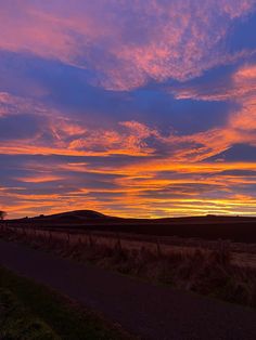 the sun is setting over an open field with hills in the distance and clouds in the sky