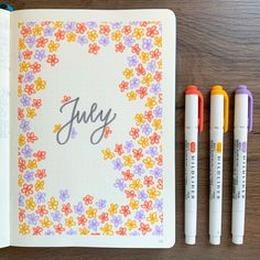 an open notebook with three markers next to it and the word july written in cursive writing