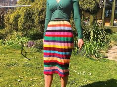 a woman standing in the grass wearing a multicolored knit skirt and green top