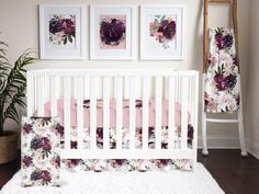 a white crib with pink and purple floral bedding next to two pictures on the wall