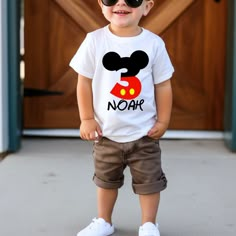 a little boy that is standing up in front of a door wearing sunglasses and a mickey mouse shirt