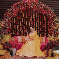 a woman sitting on top of a couch in front of a flower covered stage with lots of flowers