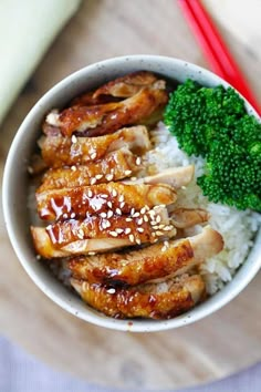 a white bowl filled with rice and chicken next to broccoli on a wooden table